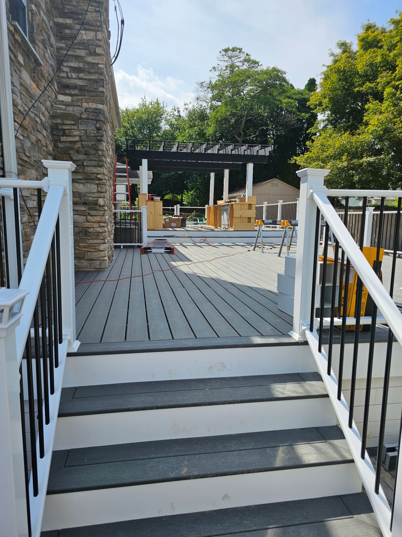 Composite deck with white railings, staircase, and pergola in the background
